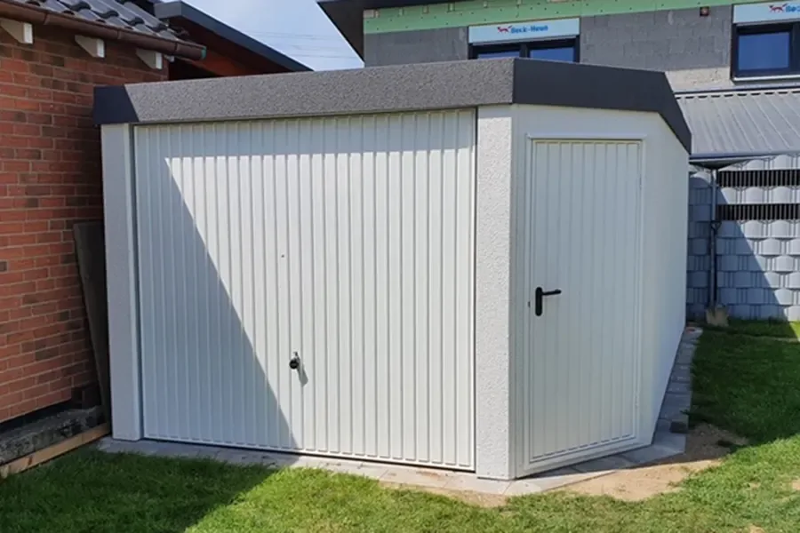 Weiße Fertiggarage mit Schwingtor und Nebentür neben einem Klinkerhaus