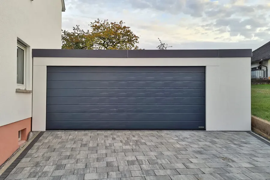 Großraumgarage mit einem breiten anthrazitfarbenen Sektionaltor neben einem Wohnhaus