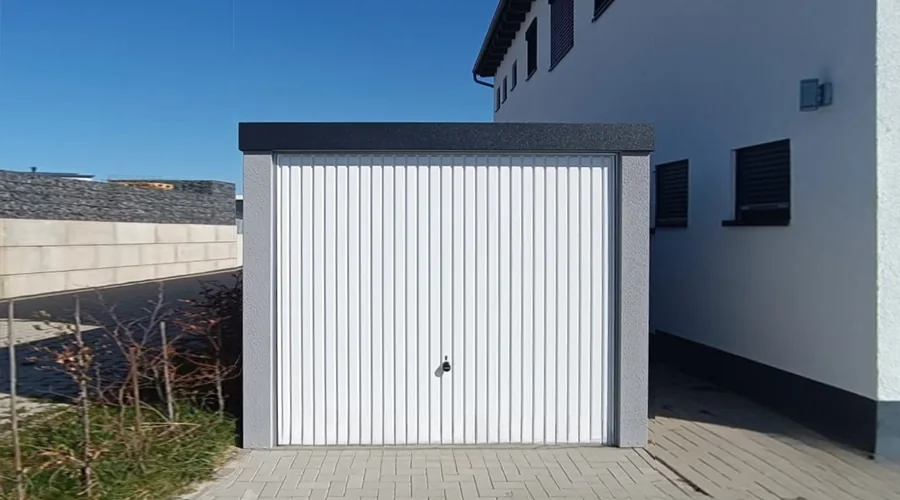 Einzelgarage mit weißem Schwingtor neben einem Wohnhaus